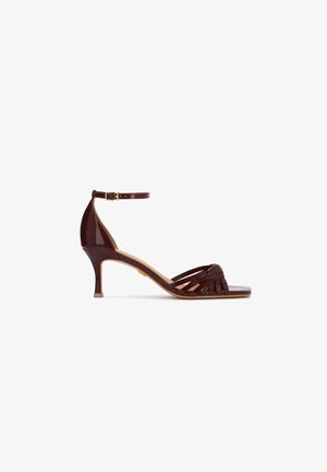 Brown leather strappy sandal with mid-height kitten heel and ankle strap with gold buckle, open toe, and woven front design.
