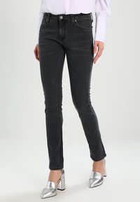 Svarta slim fit jeans med medelhög midja, med klassisk femficksdesign, dragkedja och subtilt blekt mönster. Kombineras med silverfärgade klackar.