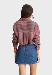 Chemise à carreaux rouge et bleu avec une coupe décontractée et des poignets à boutons, associée à une jupe en denim taille haute. Manches courtes, détail de pli au dos.