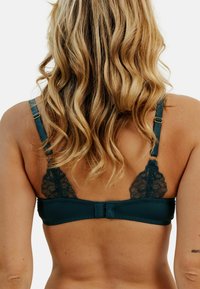 Soutien-gorge teal avec des accents en dentelle sur les bonnets, des bretelles ajustables avec des accessoires en or, et une fermeture à crochets au dos.