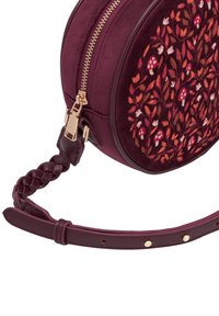Borsa rotonda bordeaux con zip dorata e manico intrecciato. Presenta un ricamo floreale in tonalità calde sulla parte frontale. Texture liscia complessiva.