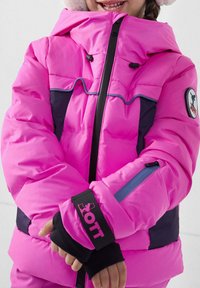 Chaqueta acolchada de color rosa brillante con capucha, laterales en azul marino contrastante, puños negros con logotipo, detalle de cremallera, textura acolchada y características ajustables.