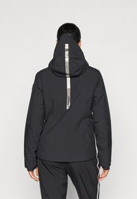 Schwarze wasserdichte Jacke mit Kapuze, ausgestattet mit einem reflektierenden silbernen Streifen auf dem Rücken und Reißverschlusstaschen. Glatte Textur, elegantes Design.