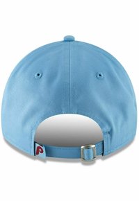 Gorra de color azul claro con textura de tela, parte posterior curvada, hebilla de metal ajustable y una pequeña etiqueta de logo en rojo en el lateral.