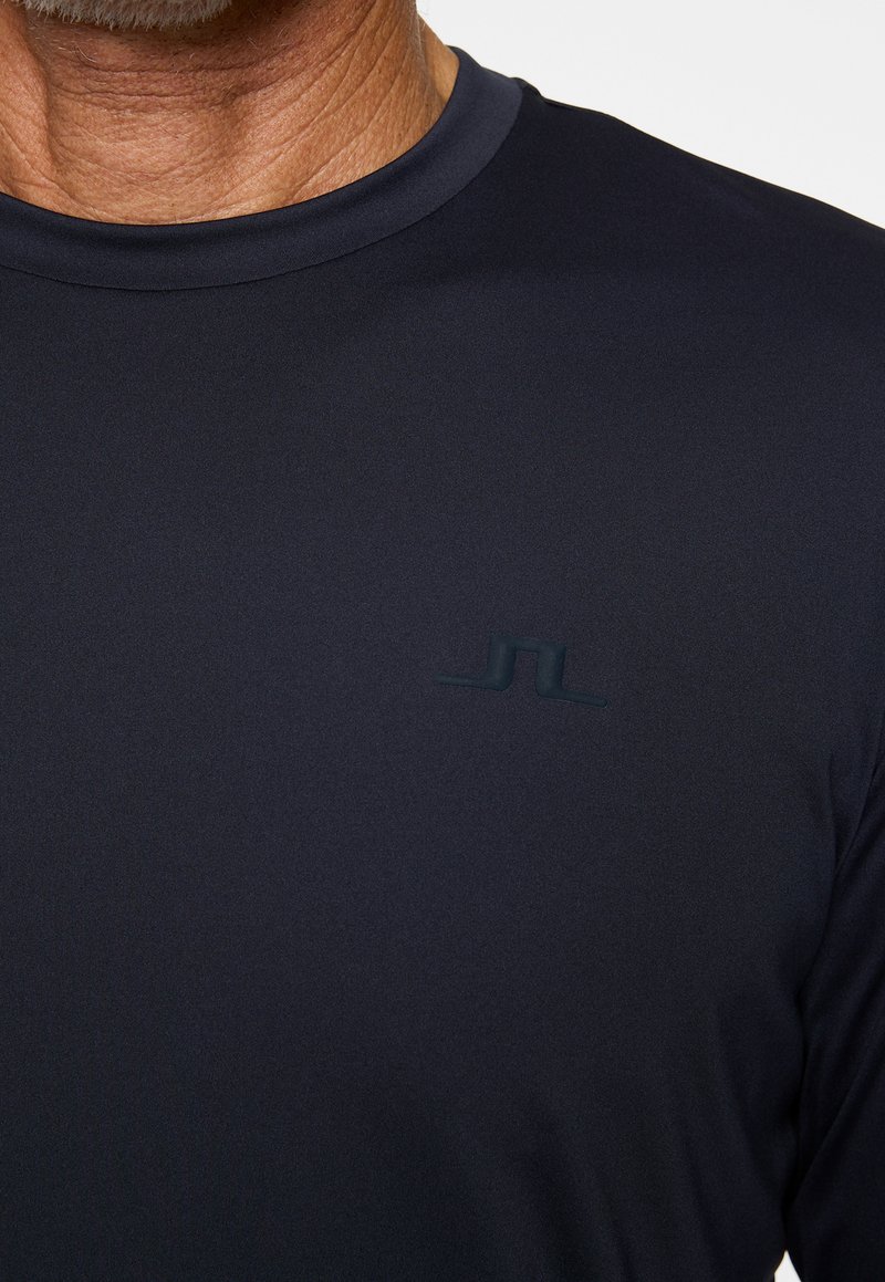 Marineblå atletisk t-shirt med korte ærmer og rund hals. Har et subtilt tekstureret stof og et lille logo i midten af brystet.