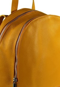 Geel leren rugzak met twee ritscompartimenten, ronde vorm en gestructureerd oppervlak. Inclusief metalen ritsen met zilveren accenten.