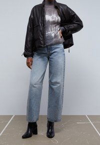 Giacca imbottita nera, maglione grigio con motivo, jeans a vita alta azzurri chiaro e stivali neri con tacco. Texture morbide e vestibilità rilassata.