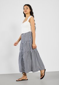 Witte cropped top met kanten schouderbanden, gecombineerd met een zwart-witte gingham maxi rok met een gelaagd ontwerp en open teen zwarte sandalen.
