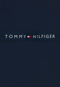 Ύφασμα σε ναυτικό μπλε με φαρδιά μπλε ζώνη και λευκό κείμενο "TOMMY" και "HILFIGER", με κόκκινες και λευκές πινελιές ανάμεσα στις λέξεις. Λείο υφή.