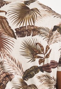 Korte mouwen, licht beige overhemd met een dicht, meerkleurig palmbladprint in tinten groen, bruin en roest. Zachte textuur.