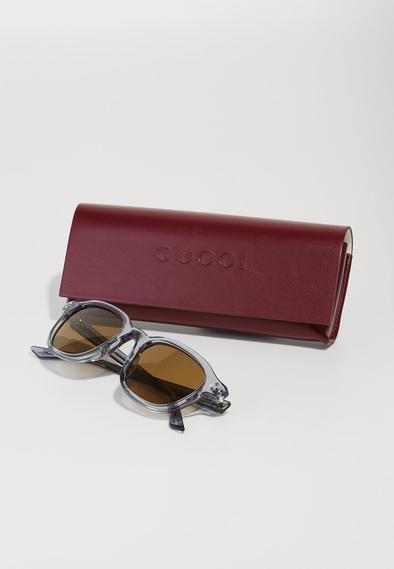 Gucci zonnebril in heldere montuur met bruine lenzen, vergezeld van een bordeaux leren etui met het merkteken erop gebosst.