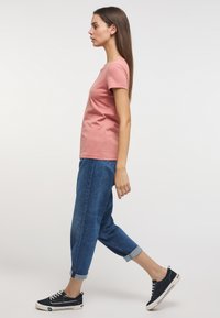 Camiseta de algodón rosa de manga corta, combinada con vaqueros de denim azul con puños doblados y zapatillas negras, mostrada en perfil lateral.