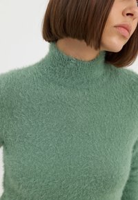 Maglione verde a collo alto, tagliato, realizzato in un morbido tessuto testurizzato con una finitura pelosa e un collo aderente.