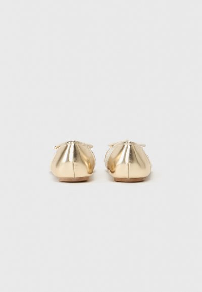 Sapatilhas de ballet douradas com um acabamento metálico suave, bico ligeiramente arredondado e um detalhe de laço decorativo na parte de trás. Sola plana, design minimalista.