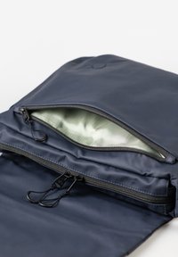 Zaino blu navy con apertura con zip, dotato di accessori in metallo neri e rivestimento interno verde chiaro. Texture liscia; materiale resistente.