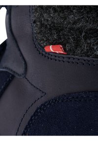 Stivale in suede blu navy con fodera pelosa grigia scura, caratterizzato da un'etichetta rossa e cuciture intricate. Primo piano sul tessuto e sui materiali.