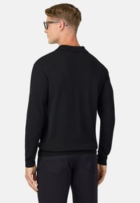 Črna polo majica z dolgimi rokavi, mehka tekstura, rebrast ovratnik in manšete, v kombinaciji s temnimi hlačami, prikazana s hrbtne strani, ki razkriva subtilne šivne detajle.