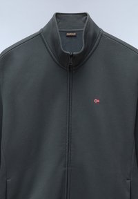 Chaqueta de cremallera gris oscuro con un cuello alto, textura sutil y una pequeña bandera noruega bordada en la parte izquierda del pecho.