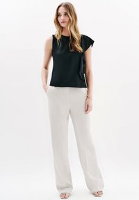 Svart ärmlös topp med volangdetaljer, matchad med ljusbeige vida byxor. Slät textur med enkel design.