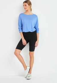 Maglietta a maniche lunghe blu abbinata a pantaloni ciclistici neri e scarpe da ginnastica argento. La maglietta ha una vestibilità comoda e un tessuto morbido. Texture liscia e design neutro.