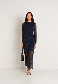 Námořnické šaty s dlouhým rukávem, vyrobené z průhledné tkaniny, s květinovým vzorem, nabíranými detaily a rovnou siluetou. Stylizované s černou kabelkou.