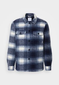 Camicia di flanella a quadretti blu navy e bianco, con colletto, chiusura a bottoni, due tasche sul petto e maniche lunghe con polsini arrotolabili.