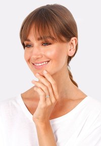 Silberner Ring mit blauen Akzentsteinen, getragen an einer Hand. Die Person hat schulterlanges braunes Haar, trägt ein weißes Oberteil und lächelt sanft.