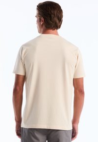 T-shirt à manches courtes beige clair en coton doux, avec un col rond et une texture lisse, présentant un dos uni.