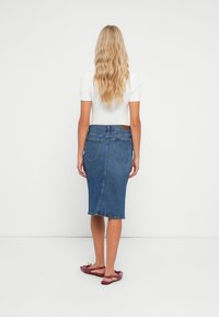 Tumši zilu džinsu svārku ar pieguļošu siluetu, līdz ceļiem sasniedzamu griezumu, aizmugurējām kabatām un etiķeti jostasvietā. Valkāta ar sarkaniem plakanajiem apaviem.