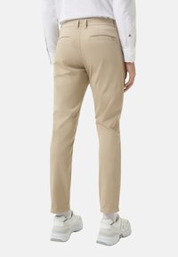 Beige chinos with a slim fit, featuring back pockets and a smooth texture. Styled with white sneakers and a button-down shirt.