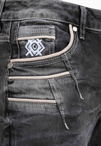 Jeans in denim nero con un distintivo design ricamato sulla tasca posteriore, con cuciture beige a contrasto e diversi dettagli sulle tasche.