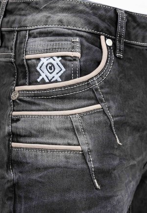 Zwarte denim jeans met een opvallend geborduurd ontwerp op de achterzak, met contrasterende beige stiksels en meerdere zakdetails.