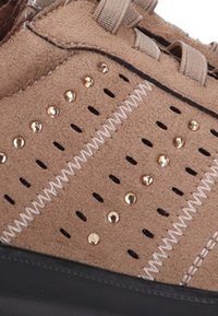 Zapato de ante marrón con diseño perforado, tachuelas decorativas doradas, costuras blancas en contraste y suela de goma negra.