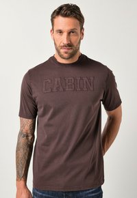 Brun t-shirt med korte ærmer og hævet "CABIN"-bogstaver på forsiden, lavet af blødt stof; kombineret med denimjeans.