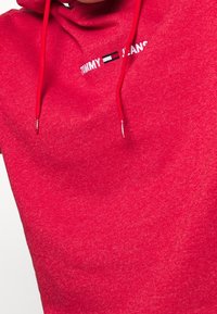 Sudadera roja con un tejido texturizado que presenta un logotipo frontal en blanco y negro. Incluye cordones para la capucha.