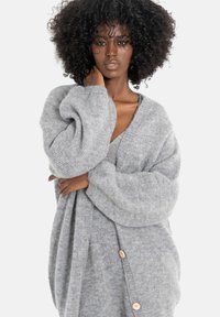 Szary oversize'owy kardigan wykonany z miękkiej dzianiny, z głębokim dekoltem w serek, dużymi rękawami i drewnianymi guzikami jako akcentami.