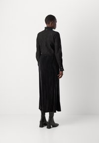 Mustat pitkähihaiset puserot, joissa on monimutkainen pitsikuvio, yhdistettynä sleek mustaan samettihelmaan. Mallilla on päällään mustat nilkkurit.