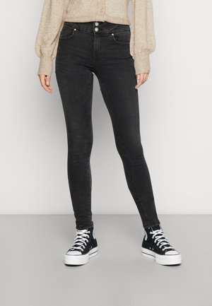 Calças de ganga skinny pretas com cintura alta, apresentando bolsos frontais, fecho de dois botões e uma textura de ganga macia. Combinadas com ténis pretos.