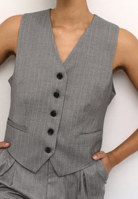 Grau gestreifter Weste mit V-Ausschnitt, fünf schwarzen Knöpfen und zwei seitlichen Taschen. Taillierte Passform mit glatter Stofftextur.