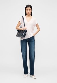 Ανοιχτό ροζ μπλουζάκι με λαιμόκοψη σε σχήμα V, τζιν παντελόνι μεσαίας μέσης σε σκούρο μπλε και άσπρα παπούτσια με μυτερό δάχτυλο, συνδυασμένα με μια μπλε τσάντα ώμου με ασημένιες λεπτομέρειες.