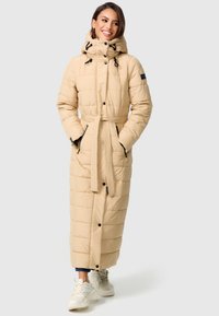 Manteau long en beige matelassé avec capuche, taille ceinturée et accents noirs. Comprend des boutons-pression et des poches latérales. Fabriqué dans un matériau lisse et rembourré.