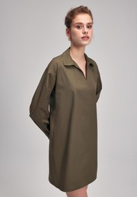 Robe verte olive à col avec manches longues, dotée d'un décolleté à mi-plateau et de coutures contrastées. Tissu lisse et léger.