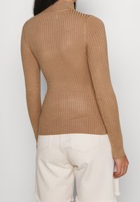 Pull à col roulé côtelé beige avec manches longues, présentant une coupe ajustée et une texture subtile, assorti à un short blanc cassé.