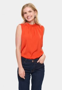 Blusa arancione senza maniche con scollatura arricciata, abbinata a jeans blu scuro con chiusura a bottone e tasche classiche.