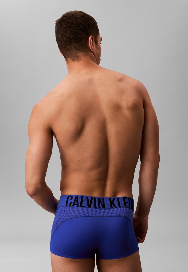 Blauwe boxershorts van elastische stof met een zwarte tailleband waarop het "CALVIN KLEIN" logo staat. Glad textuur en aansluitend ontwerp.