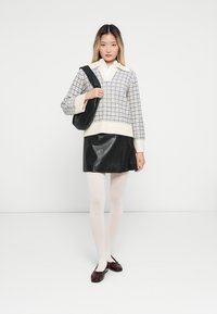 Maglione lavorato a maglia con un motivo geometrico blu e avorio, gonna di pelle nera, collant bianchi e ballerine in vernice bordeaux, abbinati a una borsa nera.