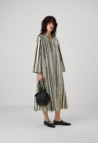 Rochie lungă, stripedă, din material crem și negru, cu decolteu în V și mâneci largi. Pur sărbătă cu pantofi plate negri și o geantă mică neagră.