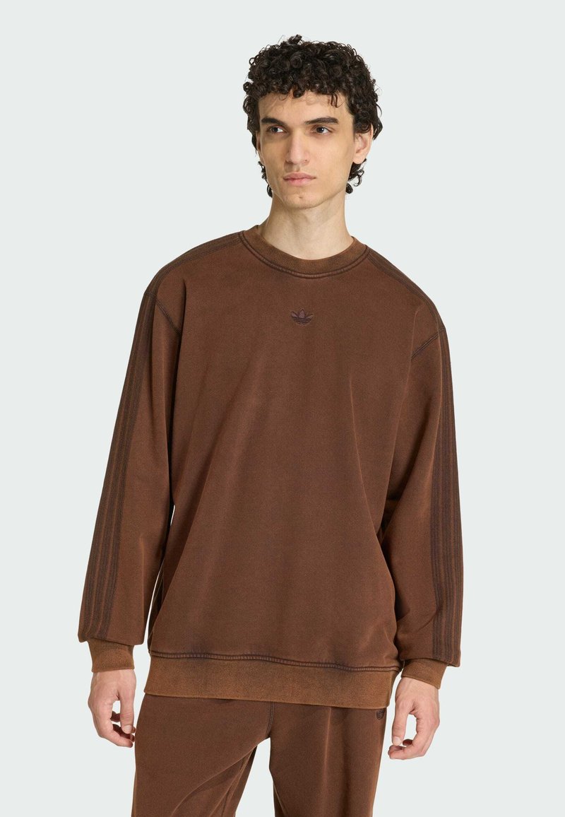 Hnedá mikina s okrúhlym výstrihom, mäkká textura, rebrované manžety a vyšívané logo na hrudi. Obsahuje tri pruhy pozdĺž rukávov.