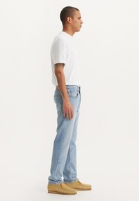 Lichtblauwe denim jeans met een rechte snit, gedragen met een wit t-shirt en tan moccasinschoenen. Kenmerken zijn onder andere achterzakken en minimale details.