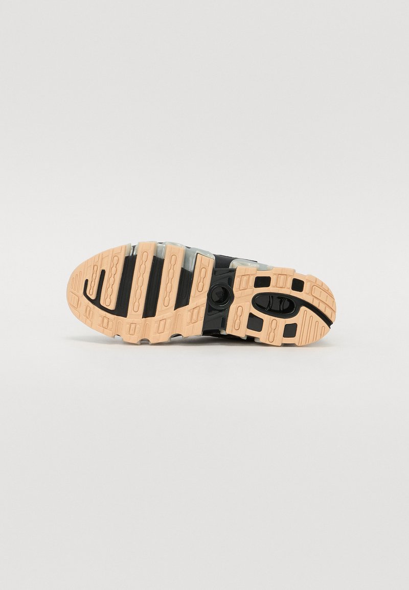 Suela de zapato con un empeine negro y gris claro, que cuenta con una suela de goma texturizada en marrón claro con patrones de relieve y acentos circulares.